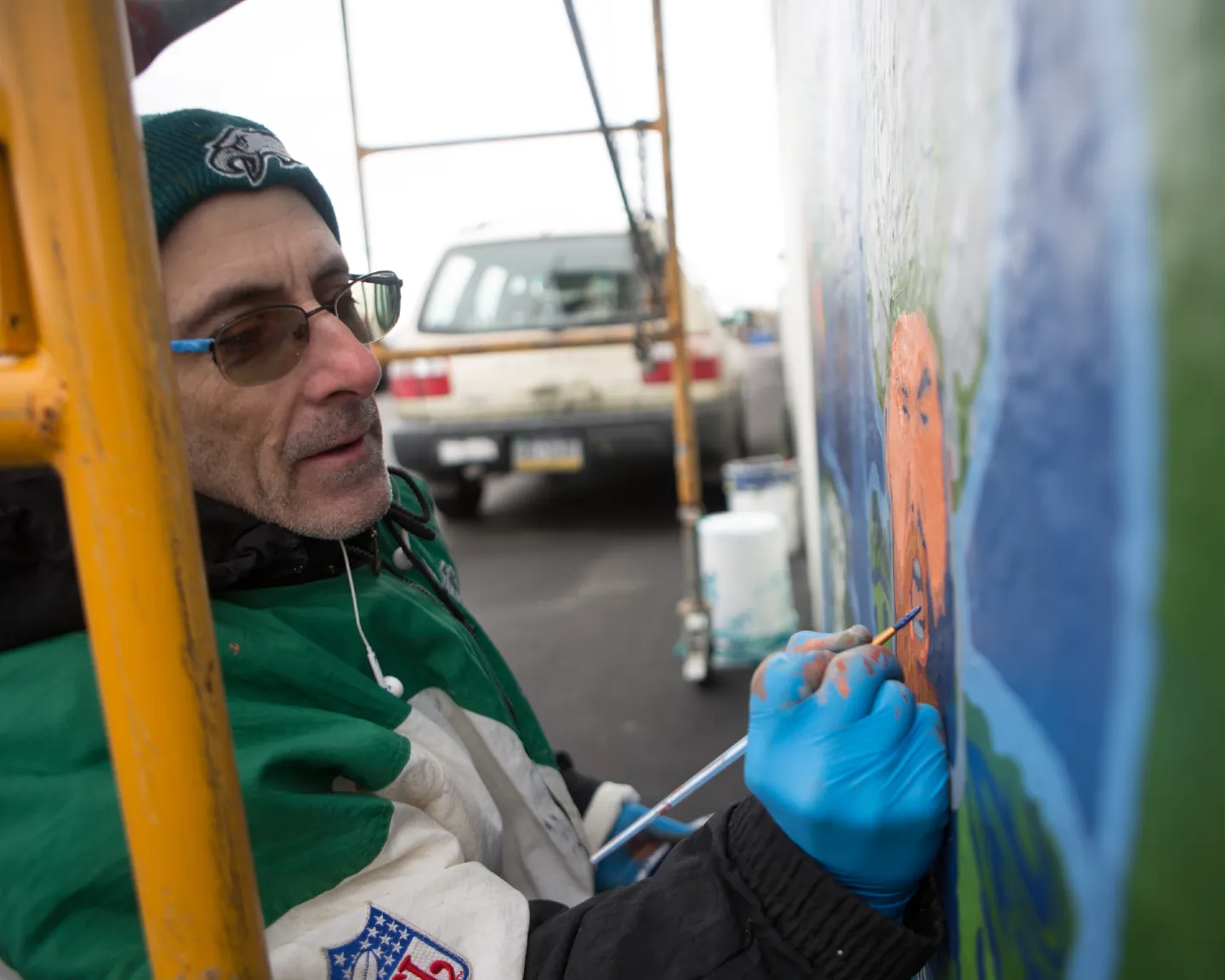 A photograph of David McShade bundled in Philadelphia Eagles winter attire, painting a mural.