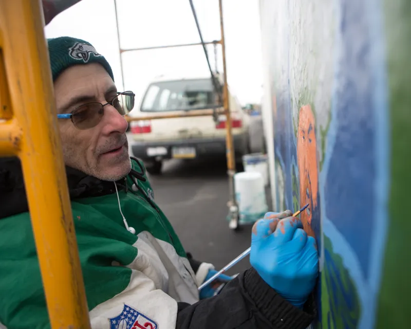 A photograph of David McShade bundled in Philadelphia Eagles winter attire, painting a mural.